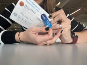 A person wearing a black and white striped sweater holds a pamphlet and a small blue and white container while sitting