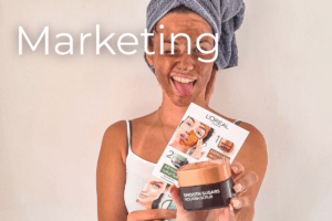 A smiling woman with a towel on her head and a facial mask holds up LOréal skincare products. The word Marketing is
