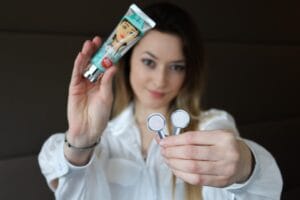 A woman in a white shirt holds up a tube of facial product in one hand and two round makeup pans in the other, focusing