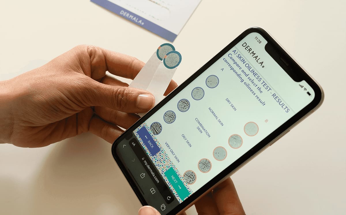 Hand Holding Skin Oiliness Test Strip While Viewing Results on Smartphone App Screen with Comparison Chart for Dry to