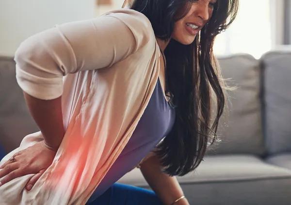 Woman holding her lower back in discomfort at home, representing the moment a consumer looks for an OTC product to solve a specific problem