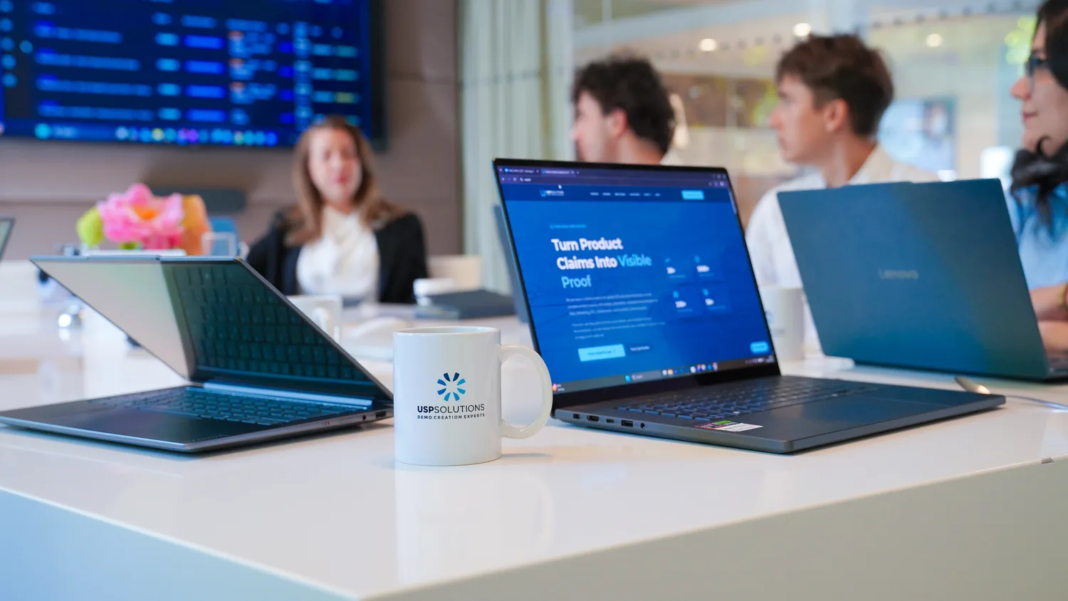 A USP Demo Solutions branded mug beside laptops showing the demo platform during a client meeting